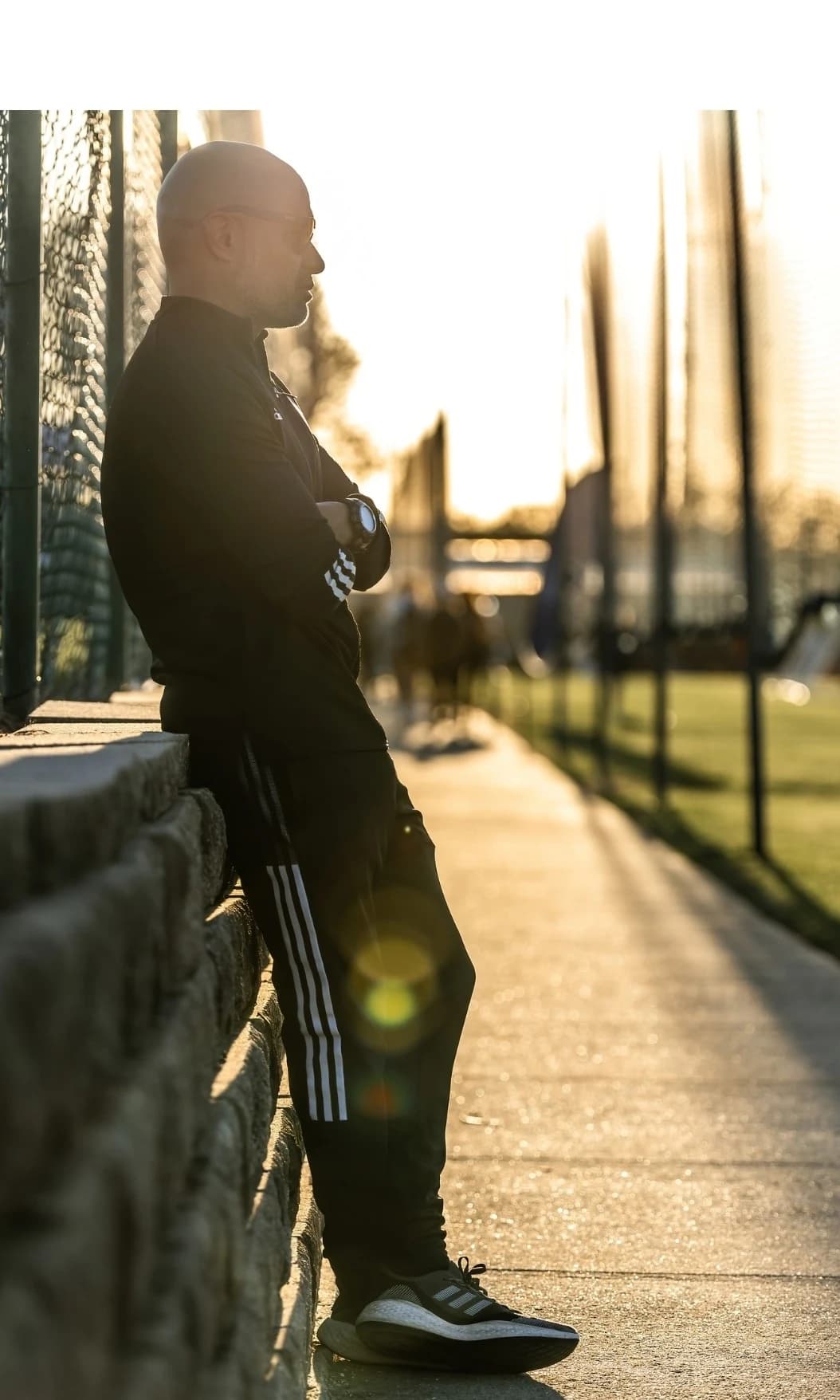 Coach Alberto Carbajal standing beside the football fields at sunset