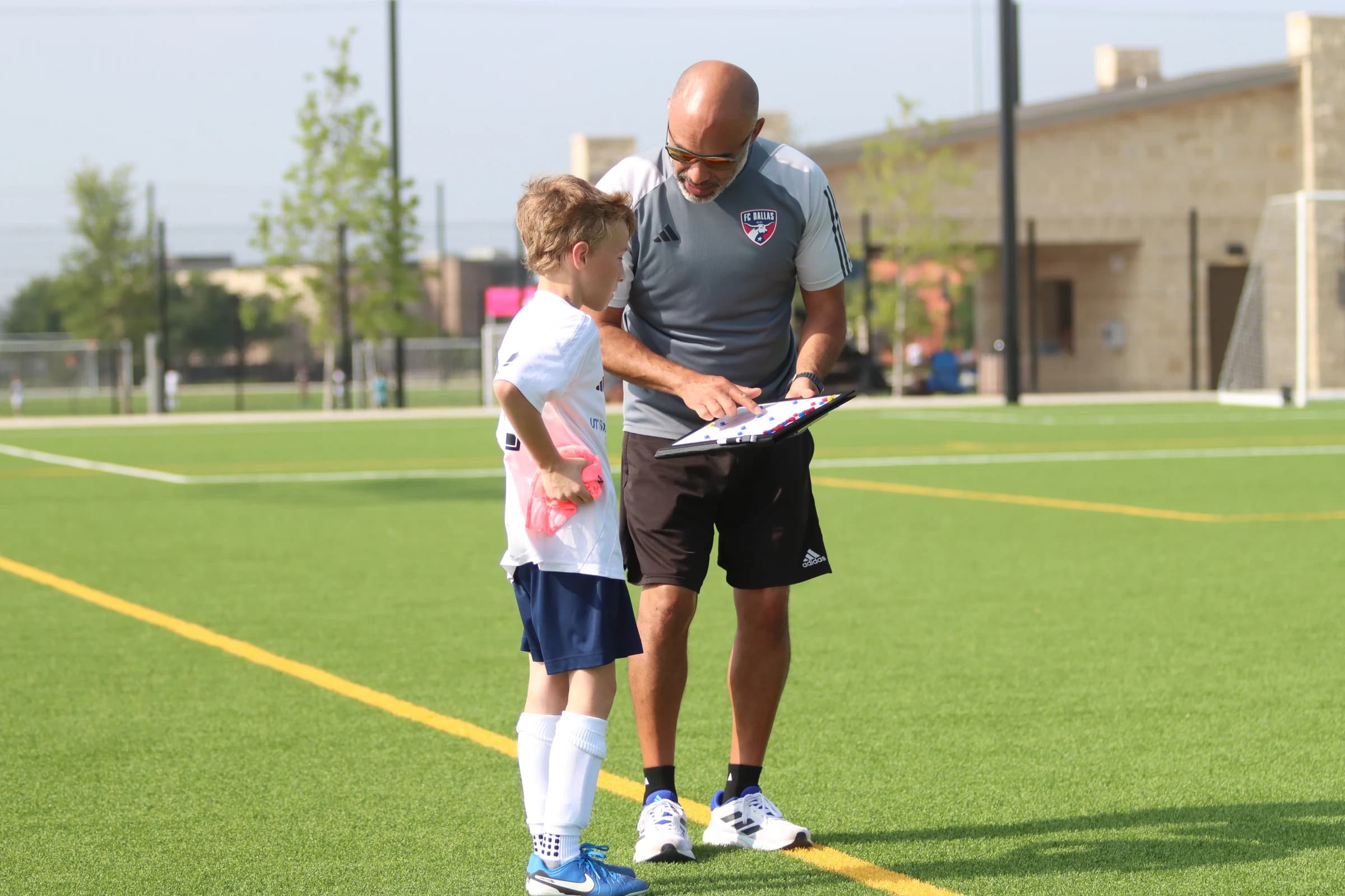 Coach Alberto Carbajal explaining a tactics board to a young footballer on the pitch