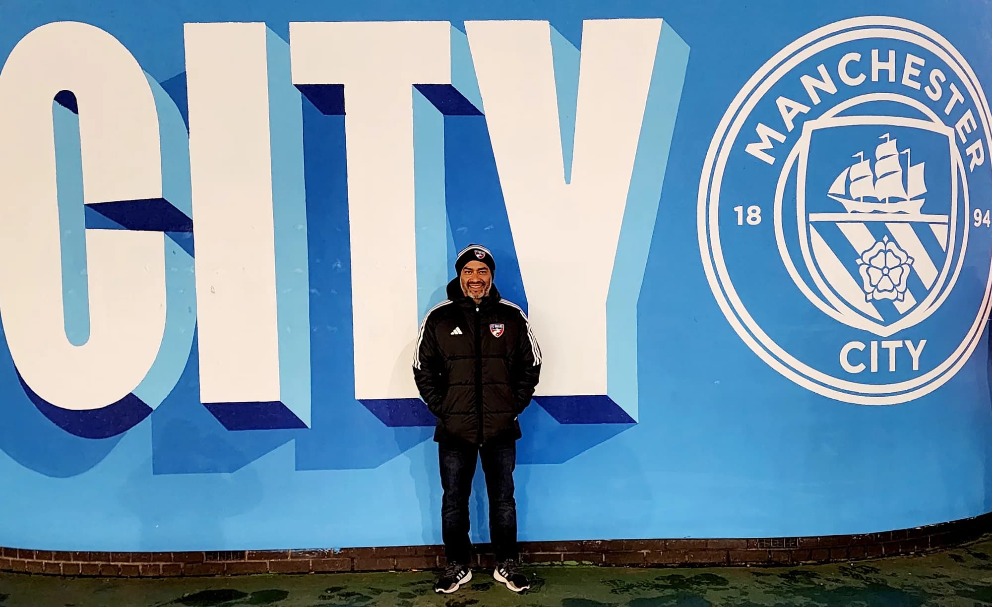 Alberto Carbajal beside a Manchester City wall display during the England team trip