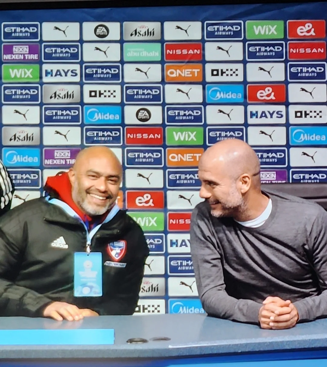 Two members of the travel group seated at a stadium media-room desk during the England visit