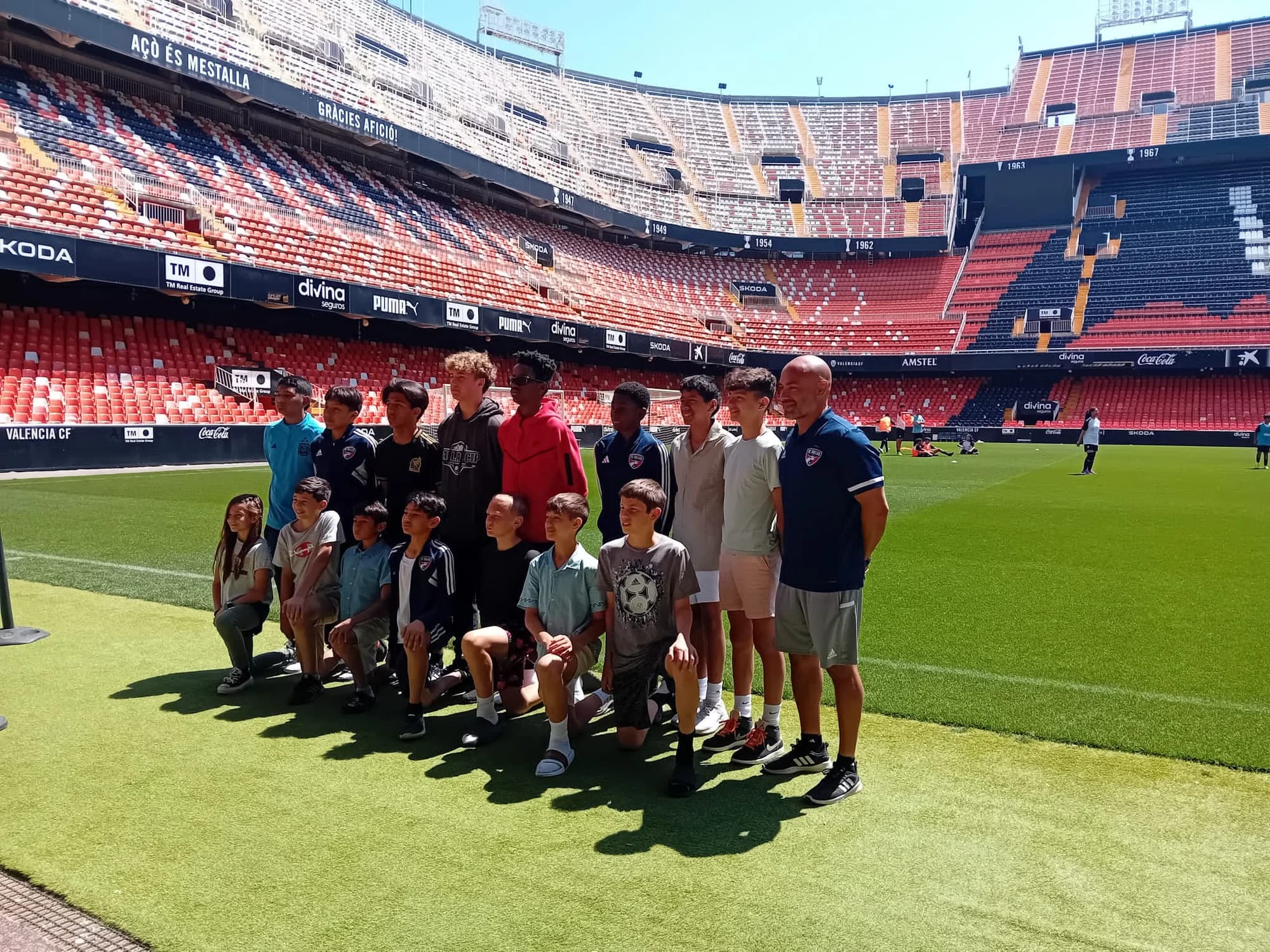 Players and coaches posing together beside the pitch inside a Spanish stadium during the 2024 team trip