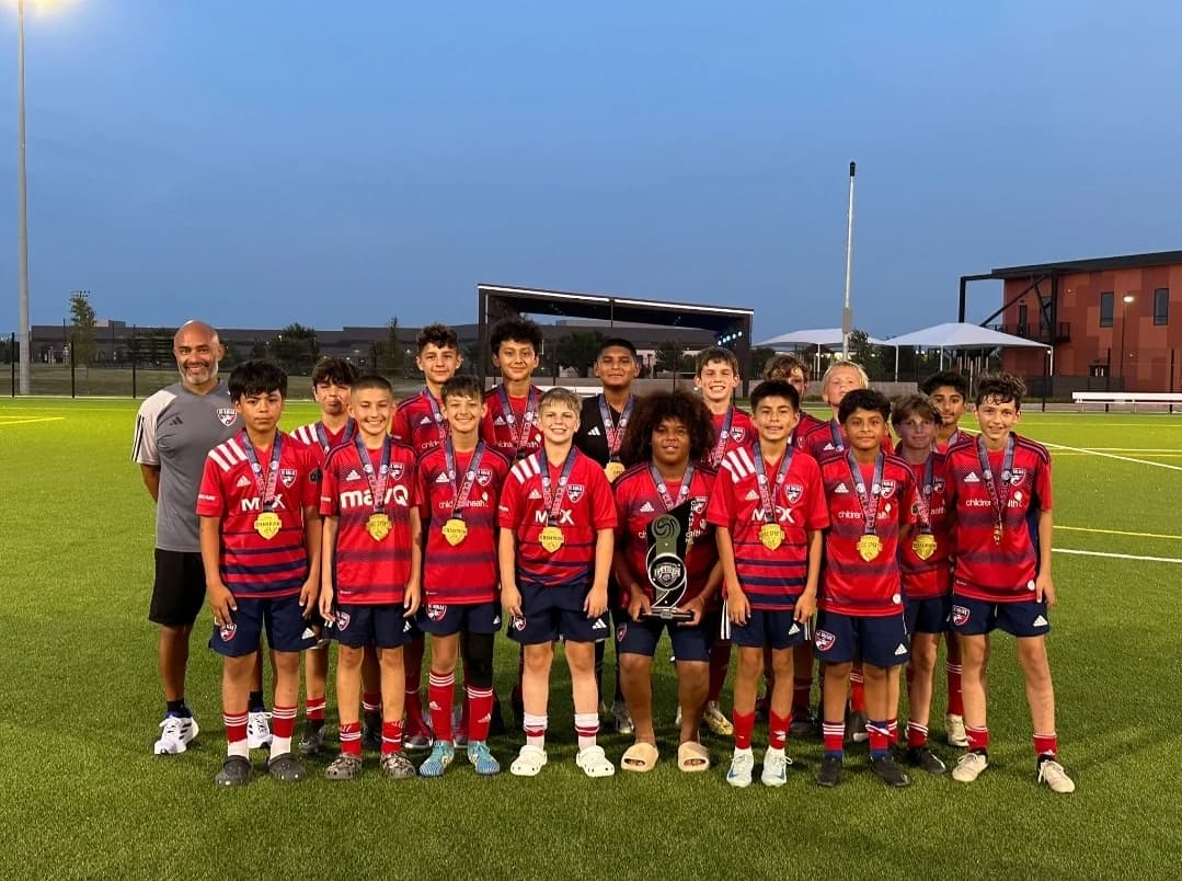 Alberto Carbajal with the FC Dallas 2011 Boys Blue ECNL RL NTX team holding a trophy and wearing medals