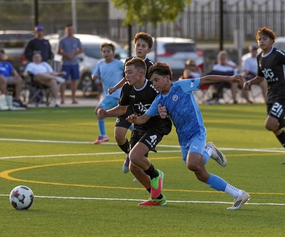 A Manchester City North Texas FC U13 player competing for the ball during a match